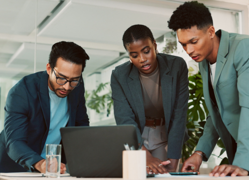 Three business professionals standing around a table, reviewing documents and data, with focused expressions