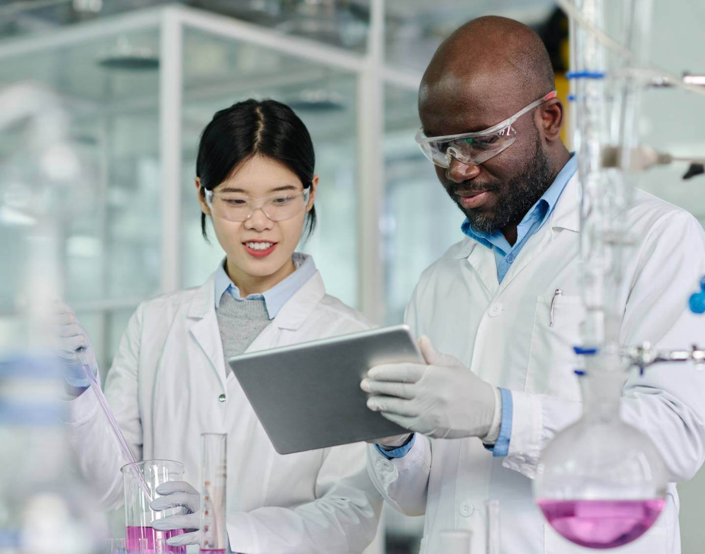 Man in lab coat looking at tablet with woman in lab coat holding flask