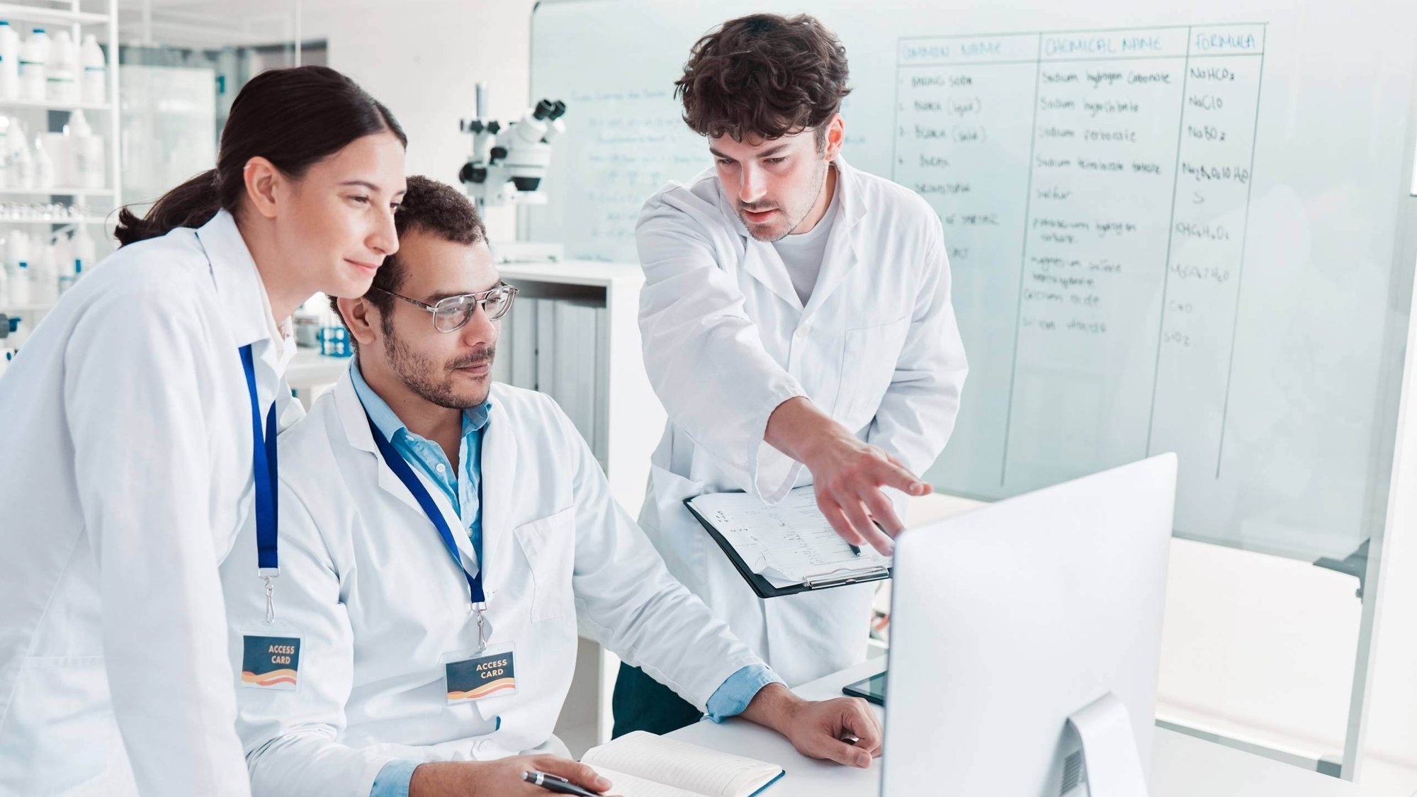 Three people in lab coats discussing data on computer screen