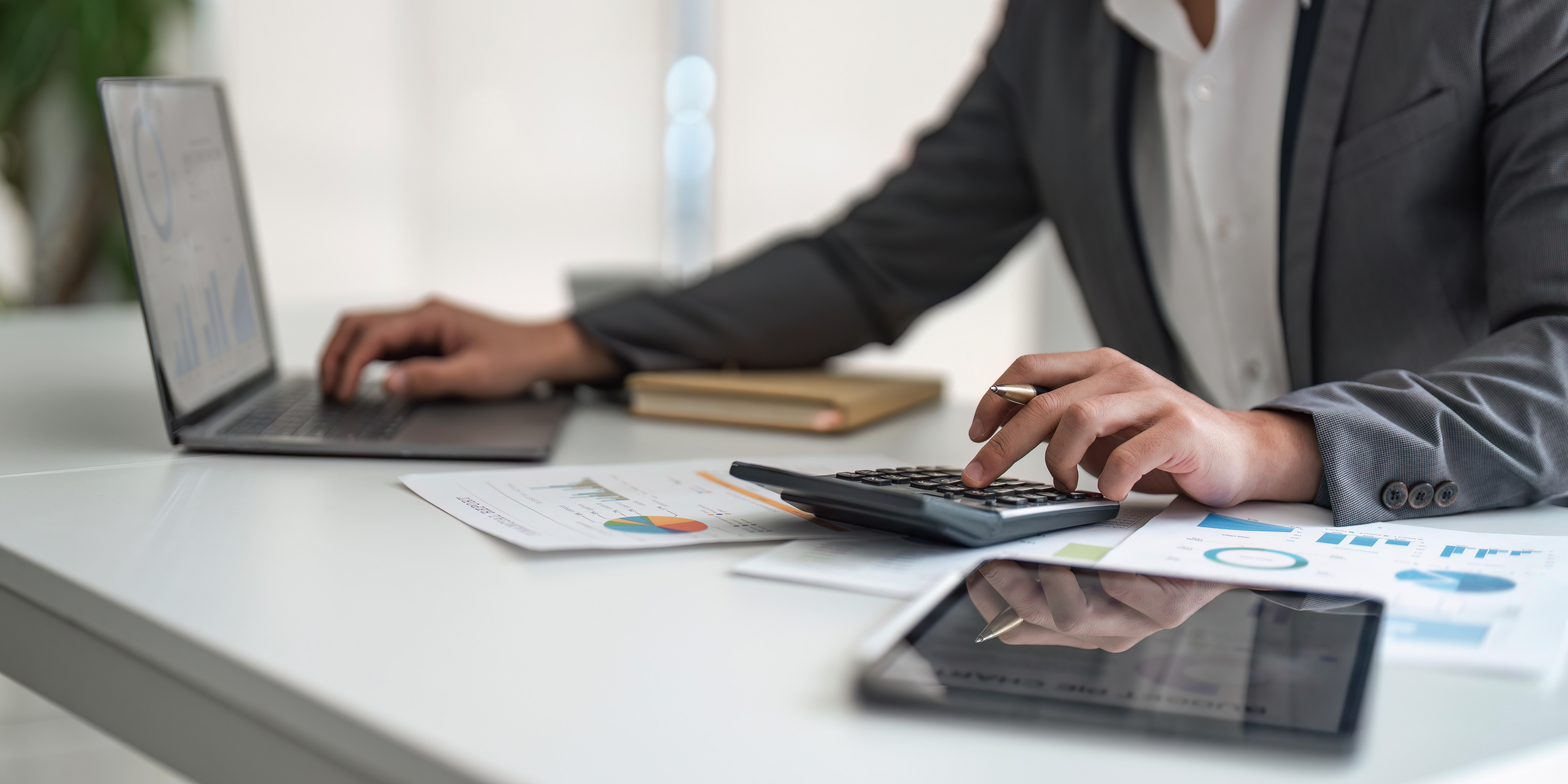 A businessman sitting at a desk, working on a laptop while using a calculator