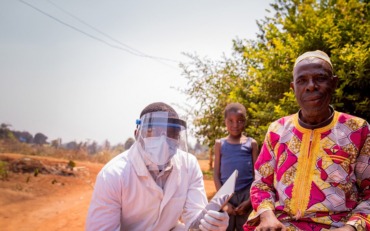 Medical personnel wearing a face shield visor sitting outdoors with a patient and their child